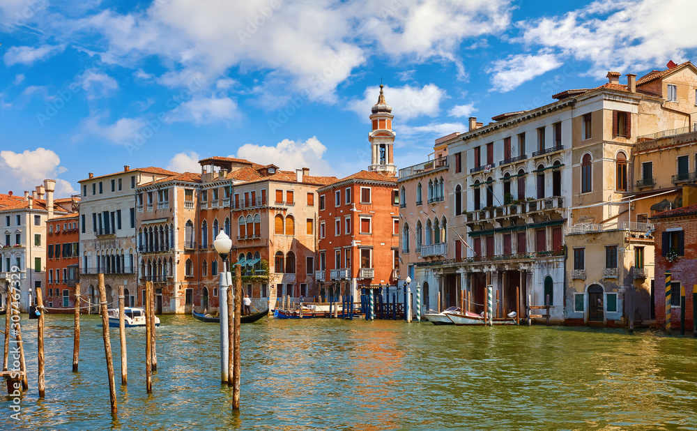 Venice, Italy. Gondolas on Grand Canal among antique buildings and traditional italian Venetian architecture. Sunny day with blue sky and clouds.