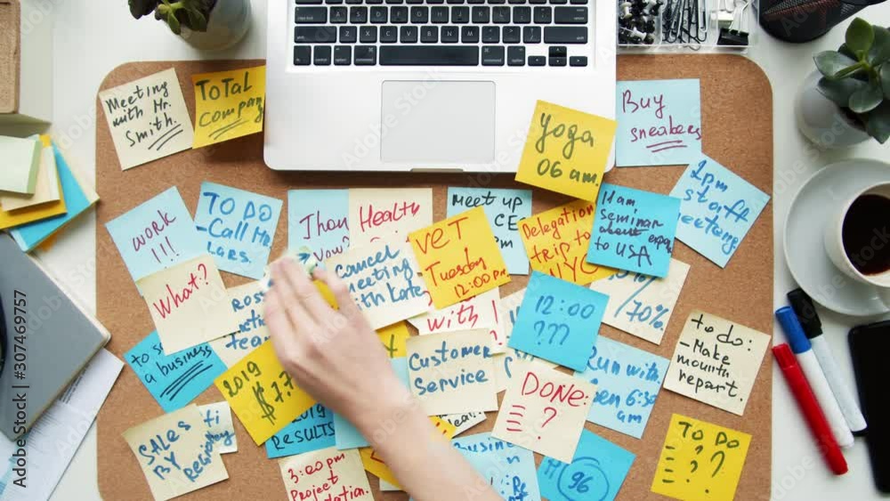 Flat lay of unrecognizable person sitting at workplace at laptop laying out colorful stickers with notes on desk