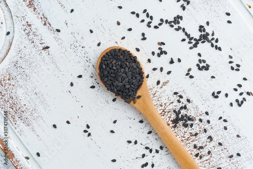 Black Sesame on wooden spoon. White wooden background. Top view, close up. Copy space.