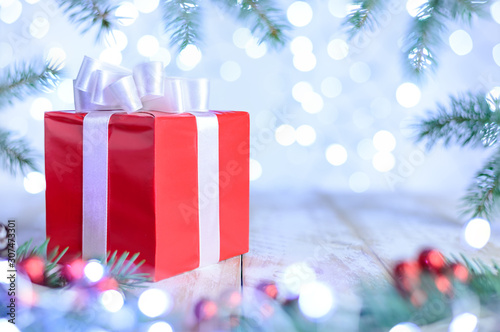 Christmas bokeh background with fir branches. A red gift box on the table with white ribbon. Copy space  soft focus.