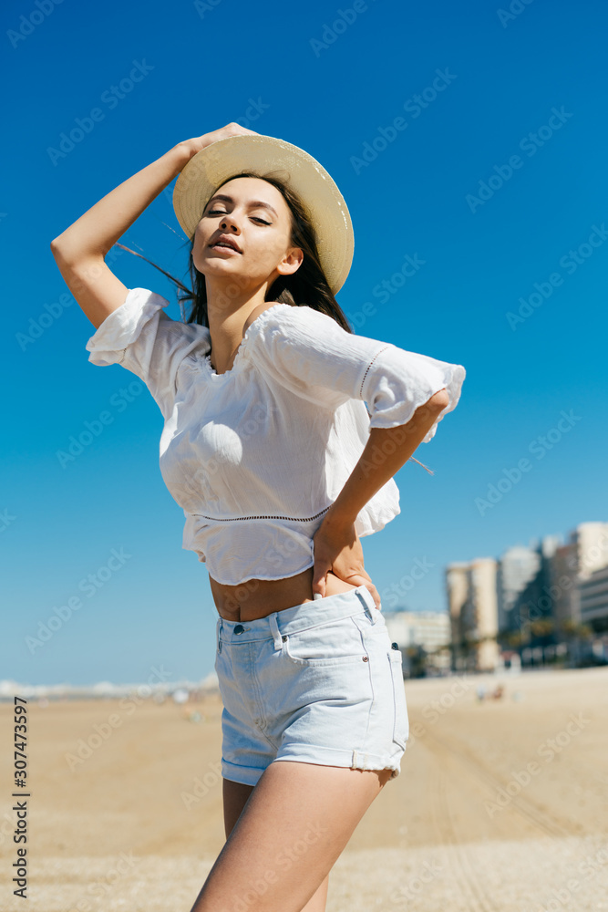 the girl in the hat, curving her back seductively, arms akimbo and holds the hat on her head with her hand, looks down the girl in the hat, curving her back seductively, arms akimbo and holds the hat on her head with her hand, looks down