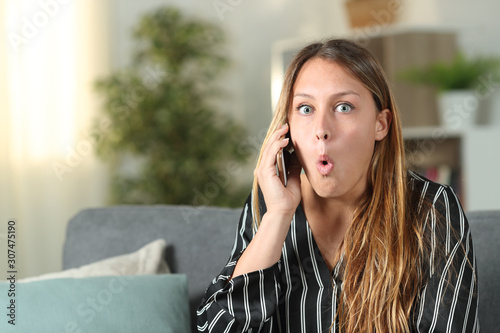 Schilderij op canvas Surprised woman talking on phone looks at camera