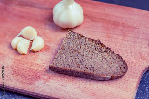 garlic soaked in a special sauce. next to a piece of dark rye bread. close-up. on a wooden background.
