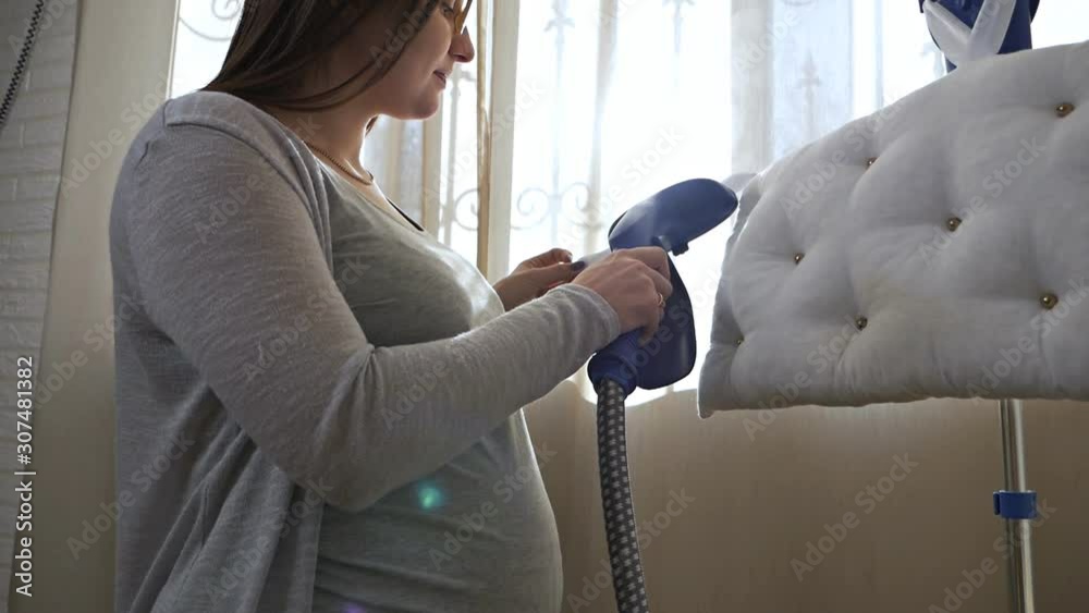 Vertical steam for clothes. Young pregnant girl in the process of