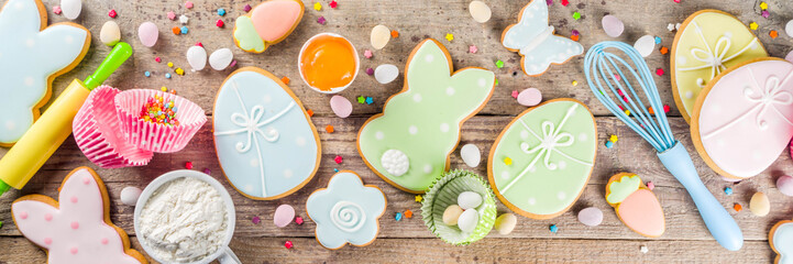 Easter cooking baking background with pastel colored easter cookies, sugar sprinkles and ingredients for bake cake and cookies.  Wooden rustic background, flatlay banner copy space