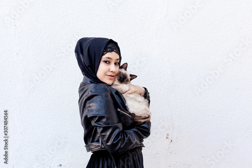 Beautiful middle-eastern Muslim woman plays with her exotic domestic Siamese cat outdoors. Pet-loving concept