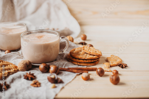 Hot cocoa with cookies, cinnamon sticks, anise, nuts on wooden background. Front view.