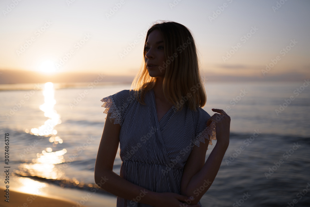 Medium shot: Portrait of a Beautiful blonde woman in a light blue dress on the Baltic Sea beach during sunset with vivid colors
