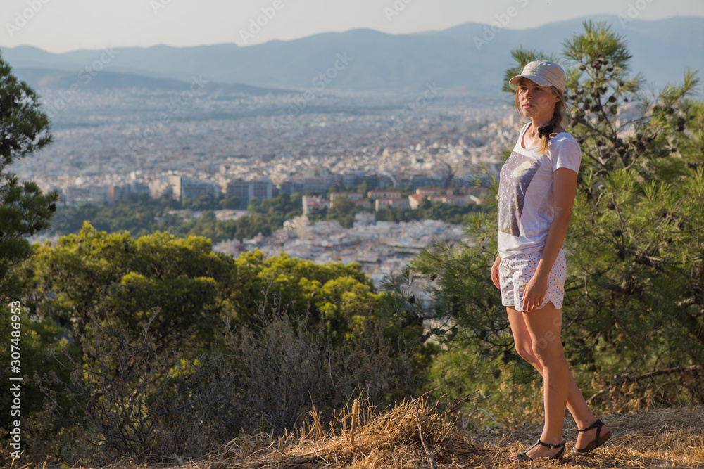 Portrait dreamy and air attractive girl in a cap being playful and carefree with beautiful smile on sunny day of the of Athens city with Mount Lycabettus, Greece as seen by air.