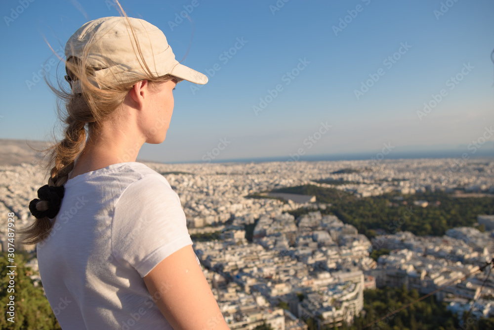Fototapeta premium Portrait dreamy and air attractive girl in a cap being playful and carefree with beautiful smile on sunny day of the of Athens city with Mount Lycabettus, Greece as seen by air.