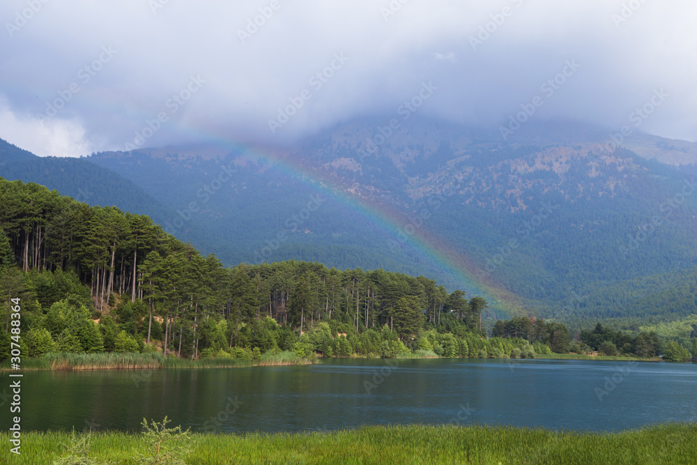 Mountain landscape. View of the blue, clean, lake Doxa and trees with rainbow (Greece, region Corinthia, Peloponnese) on a summer, sunny day.