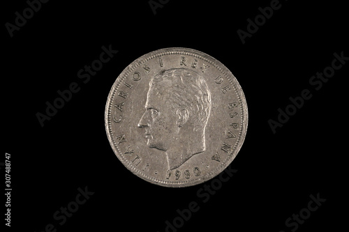 An old Spanish five peseta coin featuring Rey Juan Carlos, shot close up in macro, on a black background
