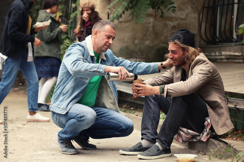 Volunteer giving drink to homeless man outdoors photo