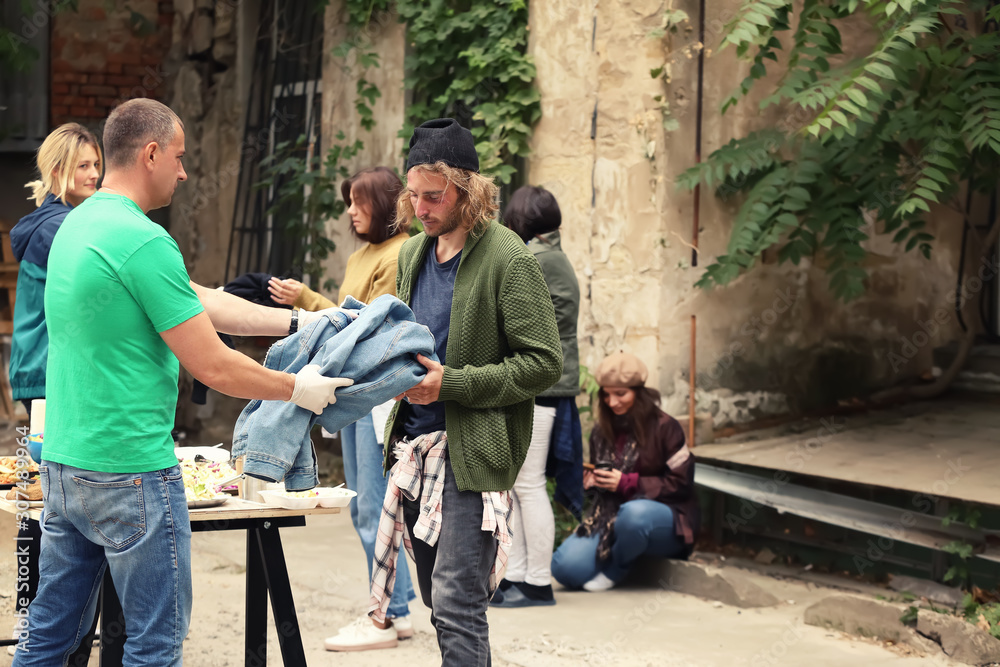 Volunteers giving clothes and food to homeless people outdoors Volunteers giving clothes and food to homeless people outdoors