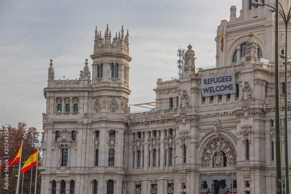 Welcome Refugee message on Palacio de Cibeles in Madrid with spain flags