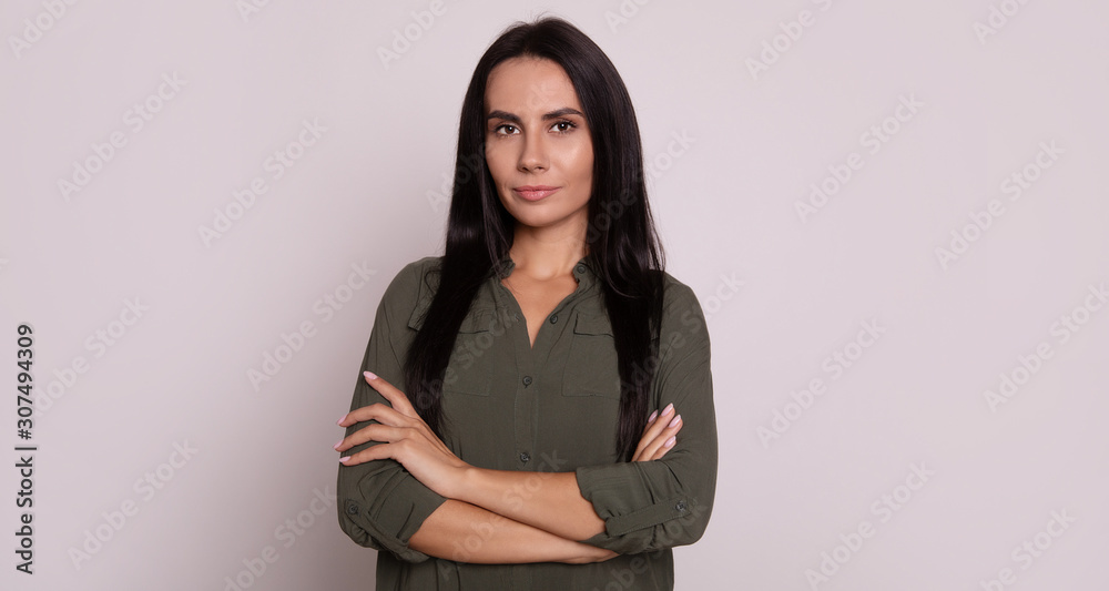 Mystery look. Close-up photo of a confident woman, who is posing in front, looking in the camera seriously with folded arms.