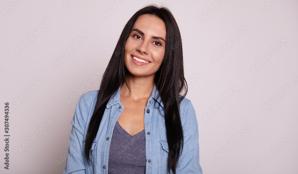 Charming smile. Close-up photo of attractive young girl in grey t-shirt and denim jacket, who is posing in front, smiling and looking in the camera with a sincere smile. Charming smile. Close-up photo of attractive young girl in grey t-shirt and denim jacket, who is posing in front, smiling and looking in the camera with a sincere smile.