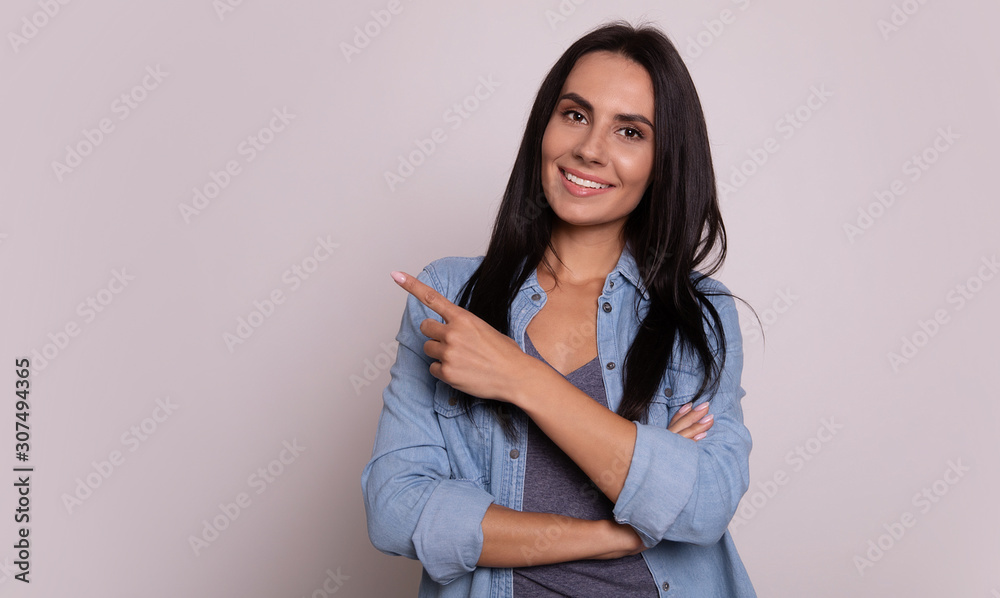 Here she is. Close-up photo of a lovely girl with long dark hair, who is smiling and posing with folded arms, pointing with her left hand to the left upper corner. Here she is. Close-up photo of a lovely girl with long dark hair, who is smiling and posing with folded arms, pointing with her left hand to the left upper corner.