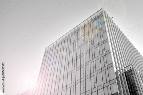 Modern office building wall made of steel and glass with blue sky. Glass surface with sunlight. Black and white.