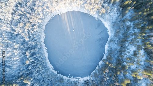 Fototapeta Naklejka Na Ścianę i Meble -  Аerial view of snow covered forest around beautiful lake. Rime ice and hoar frost covering trees. Scenic winter landscape near Helsinki, Finland.