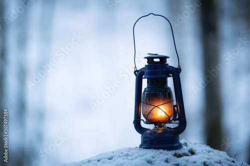 Lantern at dark in the forest at wintertime. Hiking, wilderness and peace concepts. Copy space. Blurred background. © raland