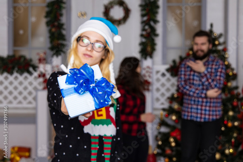 girl unfocused face giving Christmas gift to camera winter holidays concept studio photography with blurred people silhouette background