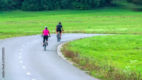 A couple is cycling on a road in the nature. They're enjoying being outdoors.