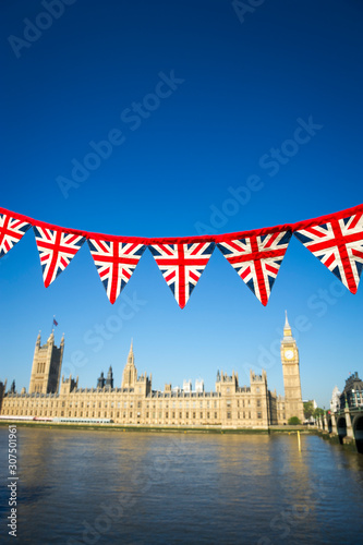 String of Union Jack flag bunting hanging in front of Big Ben at the Houses of Parliament in London, UK with bright blue sky copy space