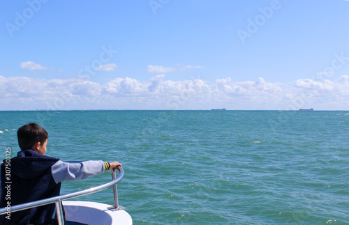 Enfant au bout d'un bateau observant l'océan, la mer est calme le ciel est joliemment nuageux
