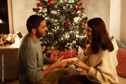 man giving gift box to woman; indoor photo with xmas decoration on background