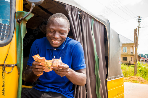 young african man driving a rickshaw taxi counting his money smiling photo