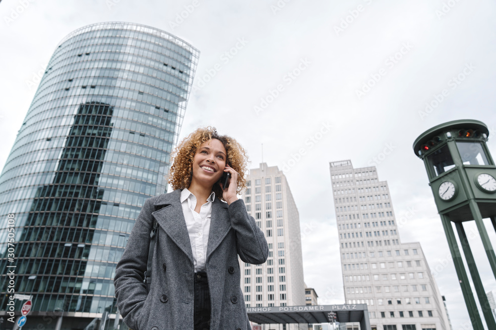 Smiling woman on the phone with office buildings in background, Berlin, Germany Smiling woman on the phone with office buildings in background, Berlin, Germany