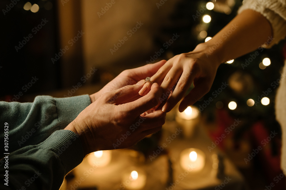 man put a ring on finger of woman; proposal of marriage;close-up couples hands with christmas background