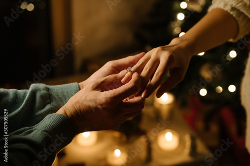 man put a ring on finger of woman; proposal of marriage;close-up couples hands with christmas background