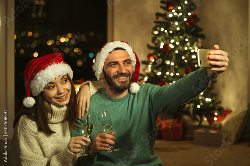 man and woman with santa claus hat holding champagne, doing selfie; christmas concept
