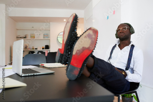 Relaxed young businessman with headphones sitting at desk in office photo