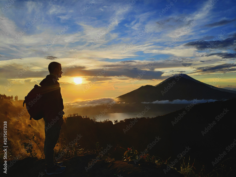 Man stays at the top of a mount with the view at Batur volcano at sunrise, early morning. Great view