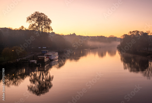 Beautiful landscape of Thames river early in the morning illuminated by colorful sunrise reflected in the foggy surface of water in London © cristianbalate