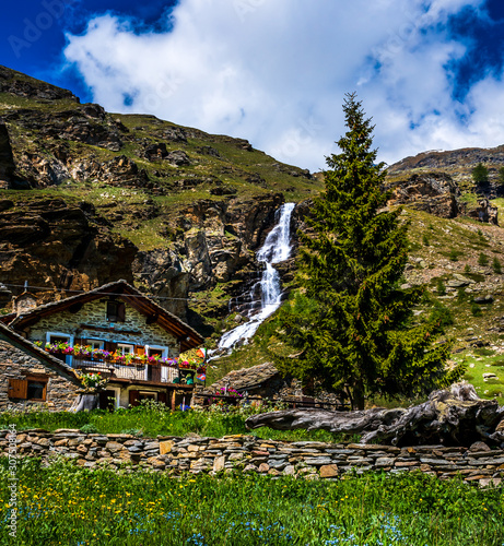 Cabin with waterfall in Gran Paradiso Italian alps mountains in Graian Alps in Piedmont, Italy with snow capped peaks.