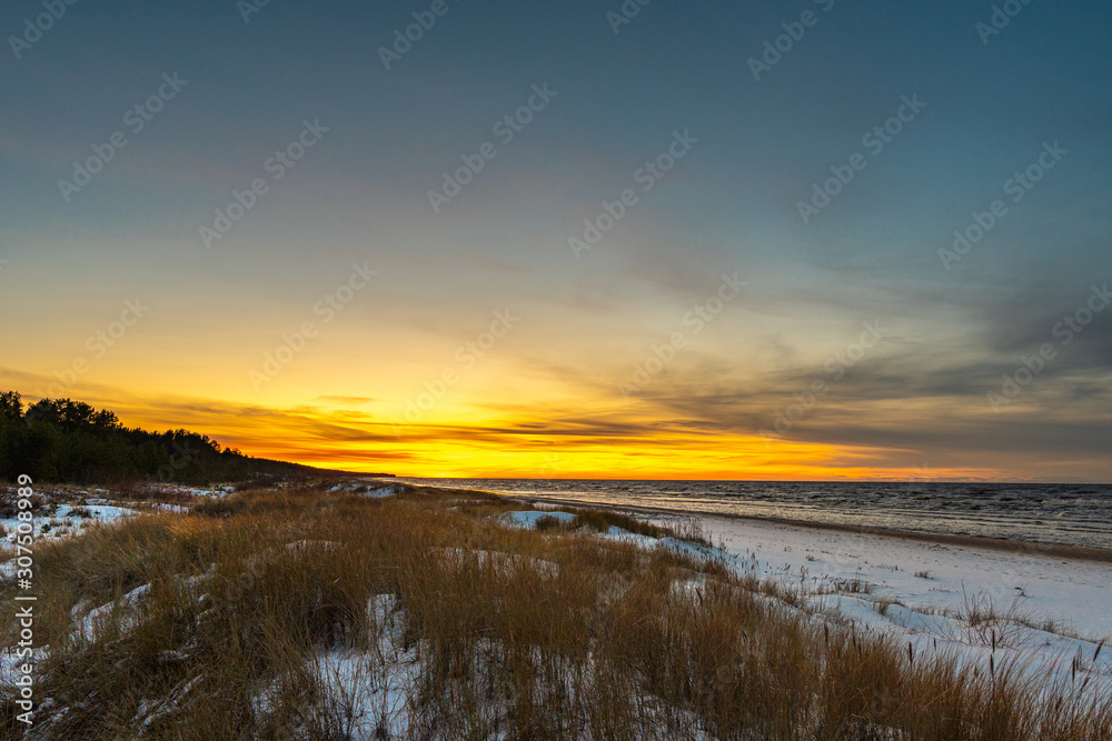 Seaside with sand dunes with snow and colorful sky at sunset, sunrise
