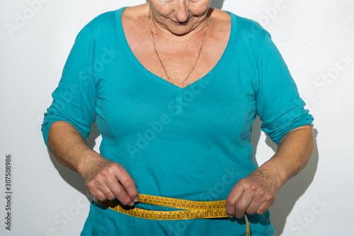 older woman body measuring her belly with yellow tape measure