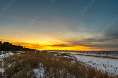 Seaside with sand dunes with snow and colorful sky at sunset  sunrise