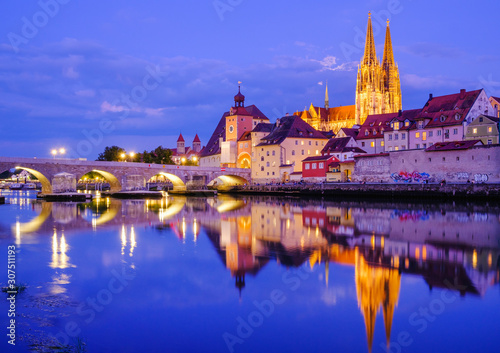 Stone bridge over Danube river in illuminated city at dusk, Regensburg, Upper Palatinate, Bavaria, Germany