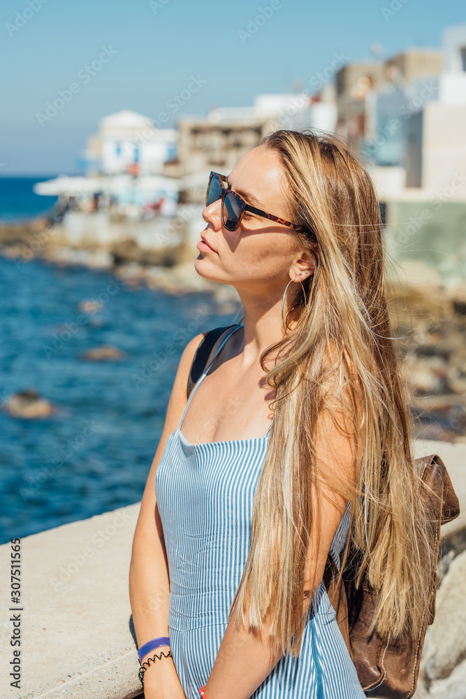 Young beautiful woman with long blonde hair in sunglasses posing by the blue sea