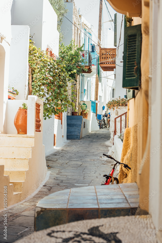 Narrow street paved with stones with tiny houses with stairs, balconies, plants and flowers at the Nisyros island