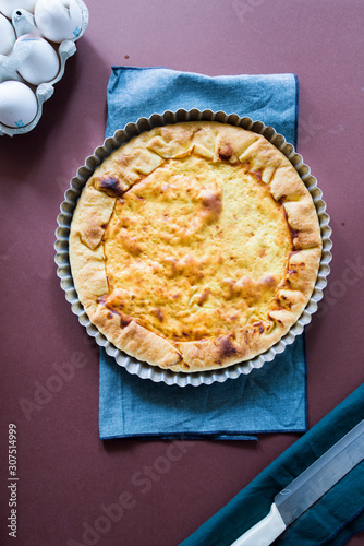 Quiche with.egg, cream, scamorza cheese and spec ham, round shaped on an aluminium mold, top view on a dark brown background