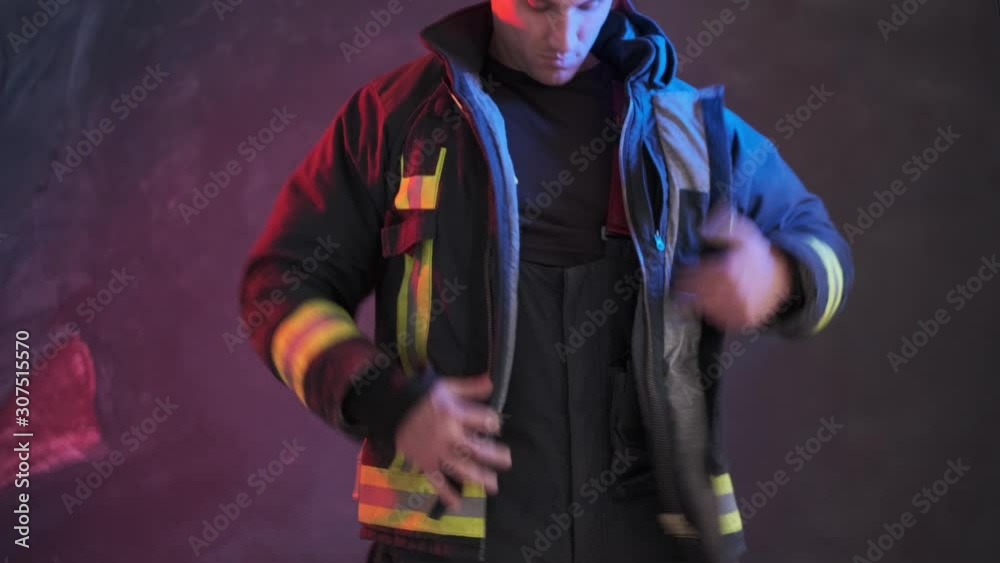 Firefighter wears uniform while standing against a gray wall Firefighter wears uniform while standing against a gray wall