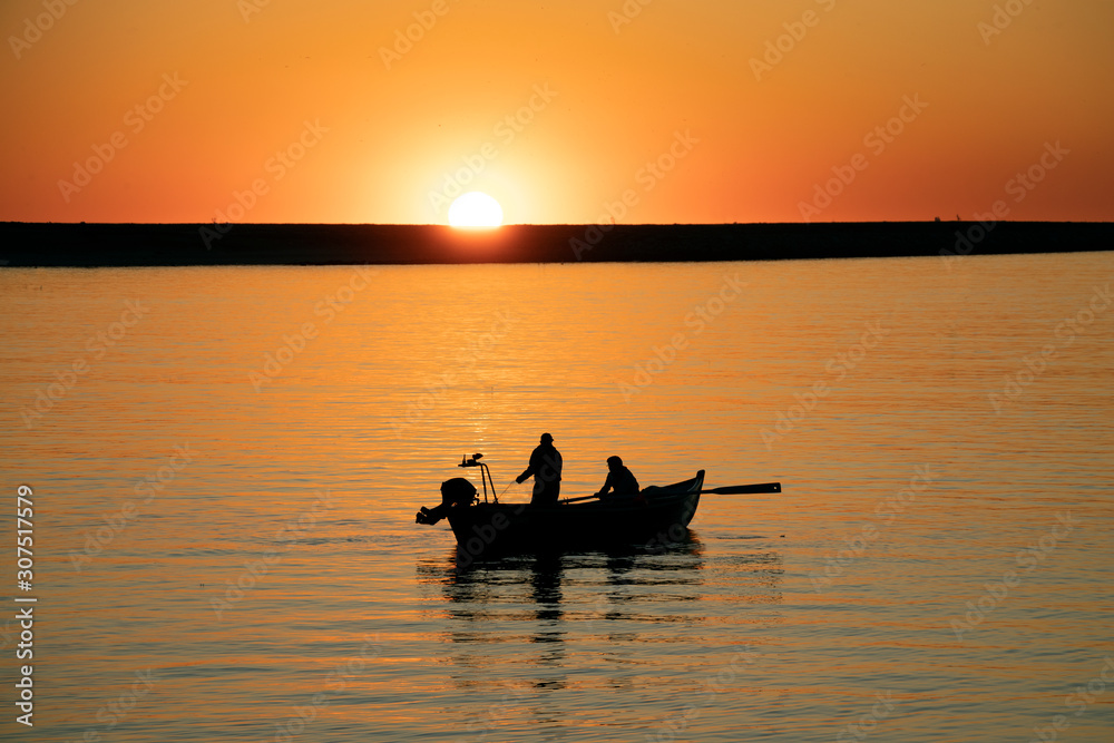 Fishermen in rowing boat at sunset in Douro River estuary, Porto, Portugal. Golden hour