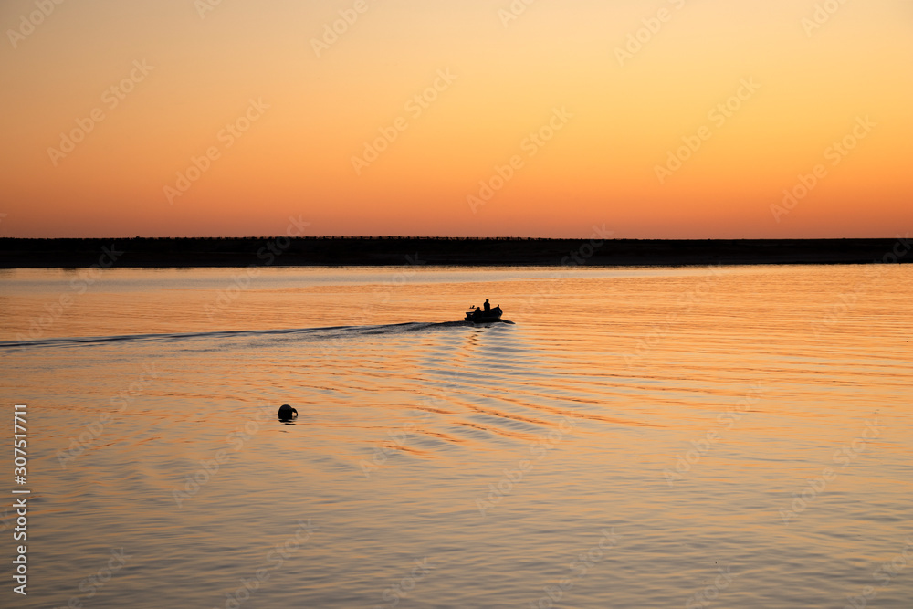 Fishermen in rowing boat at sunset in Douro River estuary, Porto, Portugal. Golden hour