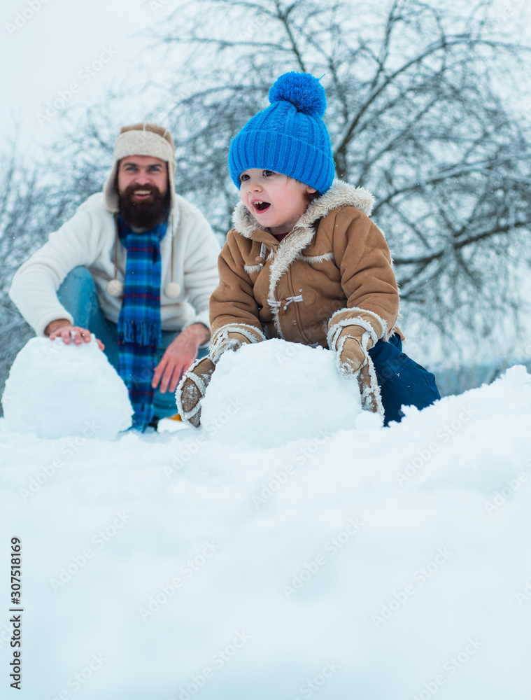 Thanksgiving day and Christmas. Cute little child boy and happy father on snowy field outdoor. Happy father and son making snowman in the snow.